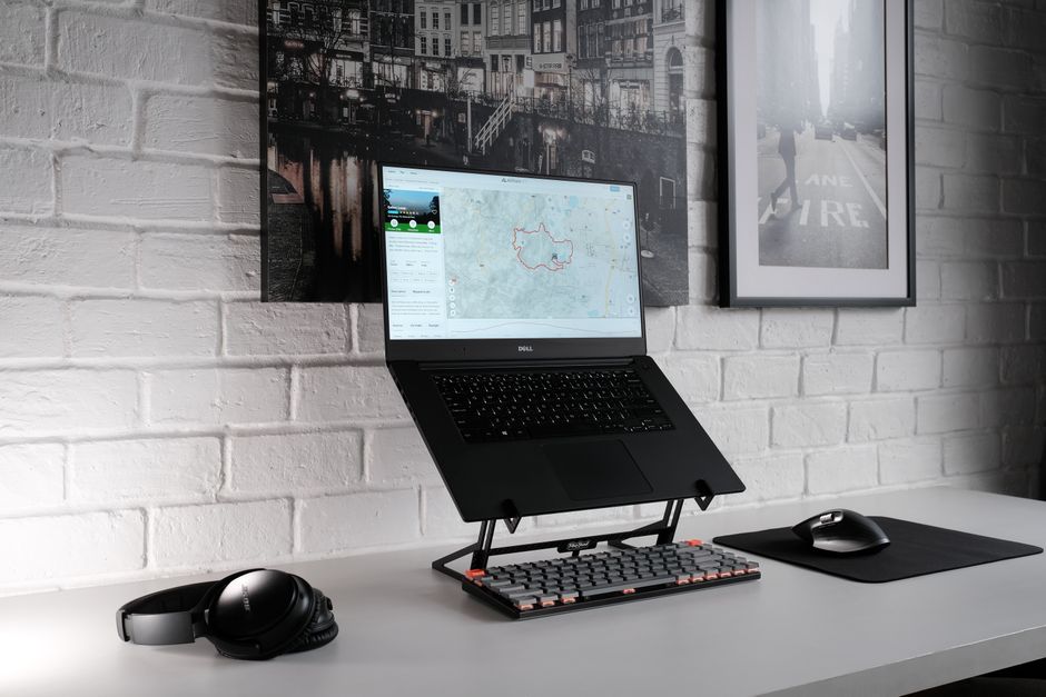 Laptop Dell na czarnej podstawce z klawiaturą mechaniczną na białym biurku.