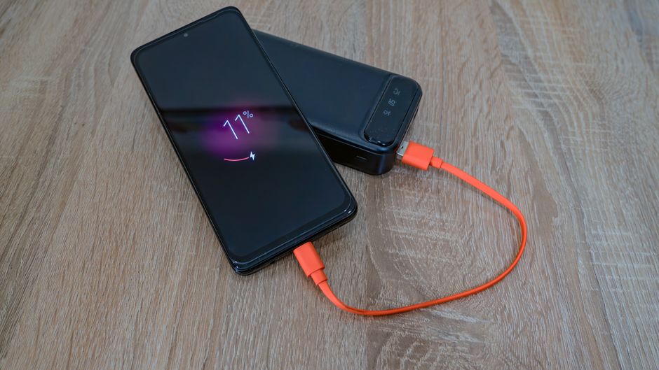 Smartfon ładowany za pomocą powerbanka przy użyciu pomarańczowego kabla USB