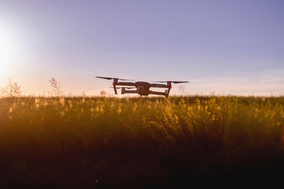 Dron unoszący się nad polem podczas zachodu słońca