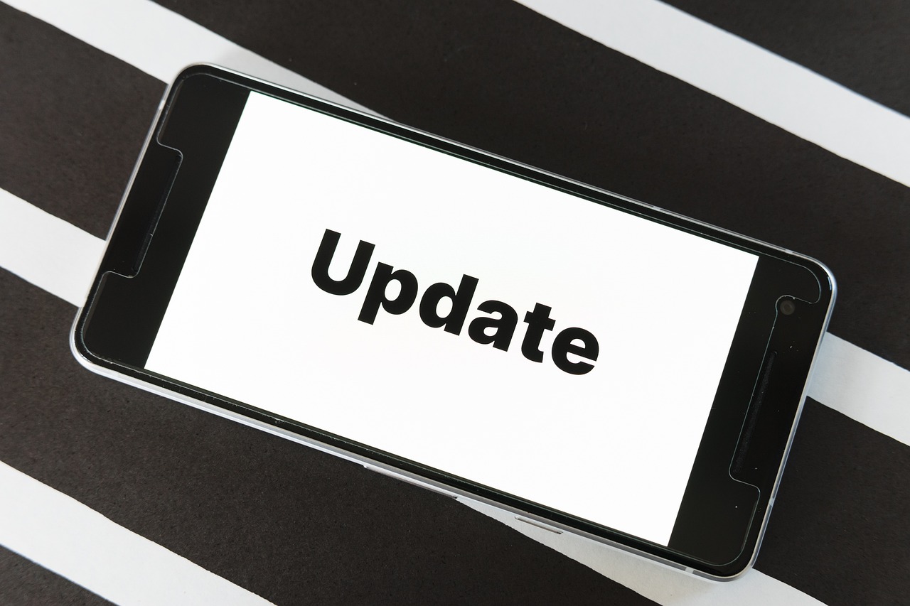 Smartfon z napisem Update na białym ekranie leżący na czarno-białych pasach.