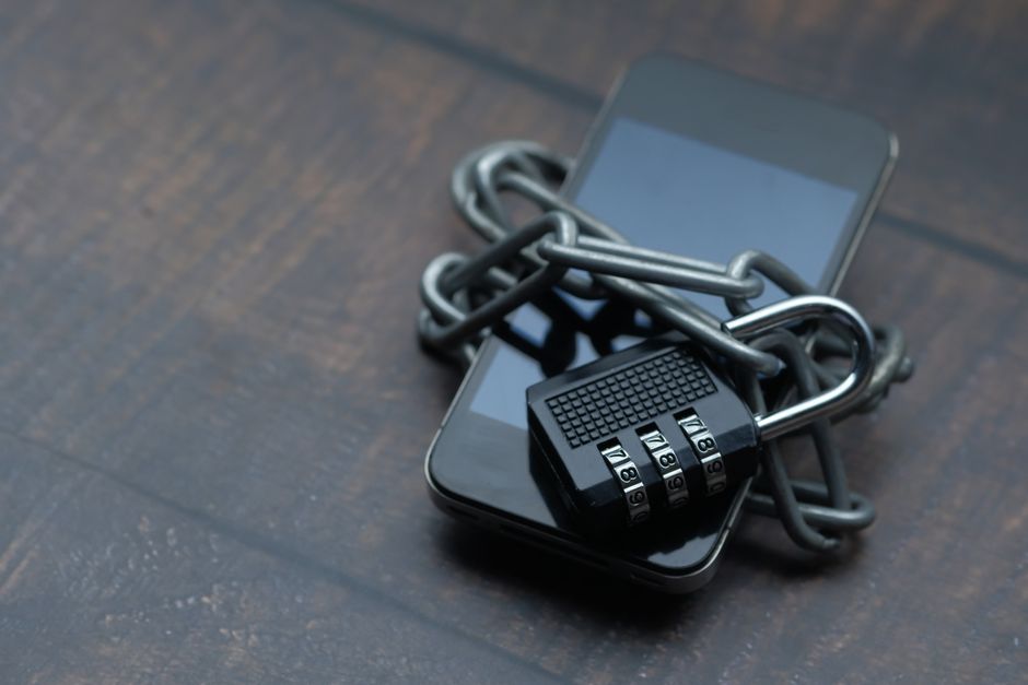 Smartfon owinięty metalowym łańcuchem zamkniętym na kłódkę szyfrową.