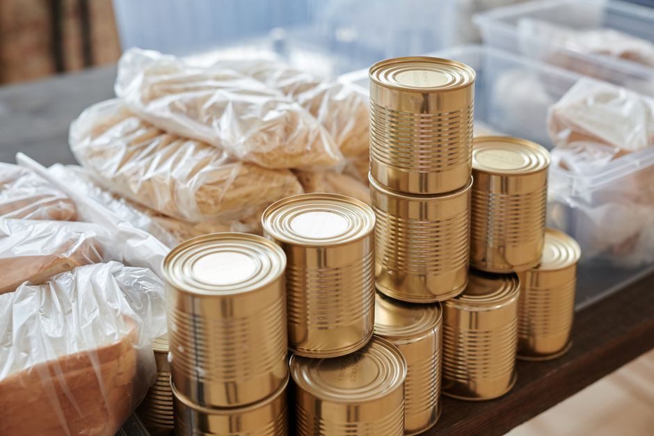 Stos metalowych puszek z żywnością obok produktów zapakowanych w foliowe woreczki.