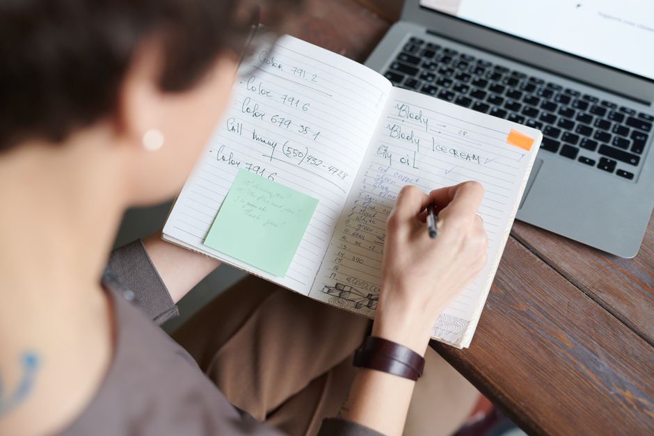 Osoba zapisująca notatki w zeszycie obok otwartego laptopa